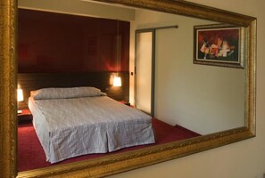 Ein Hotelzimmer mit Bett, einem Bild an der Wand und einem Spiegel, der den Raum reflektiert.