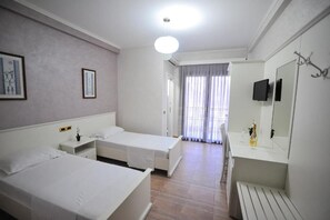 A hotel room with two single beds, a bedside table with a lamp, a TV mounted on the wall, and a bathroom with a mirror and sink. - Iliria International (Durrës)