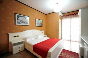 A hotel room with a bed, bedside tables, a wardrobe, and a window with curtains. - Iliria International (Durrës)
