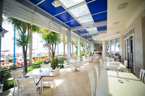 An outdoor cafe with tables and chairs, surrounded by palm trees and a view of the city. - Iliria International (Durrës)