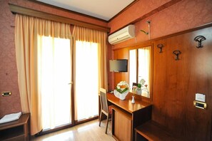 A hotel room with a wooden desk, a flat-screen TV, a large window with curtains, and a wall-mounted air conditioning unit. - Iliria International (Durrës)