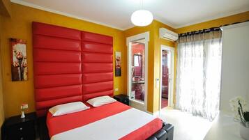 Un dormitorio con cabecera roja, cama con ropa de cama blanca y roja, una mesita de noche y una ventana con cortinas.