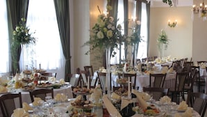 Ein formeller Speisesaal mit mehreren runden Tischen, gedeckt für eine Mahlzeit, jeweils mit weißen Tischdecken, gefalteten Servietten und Gläsern.