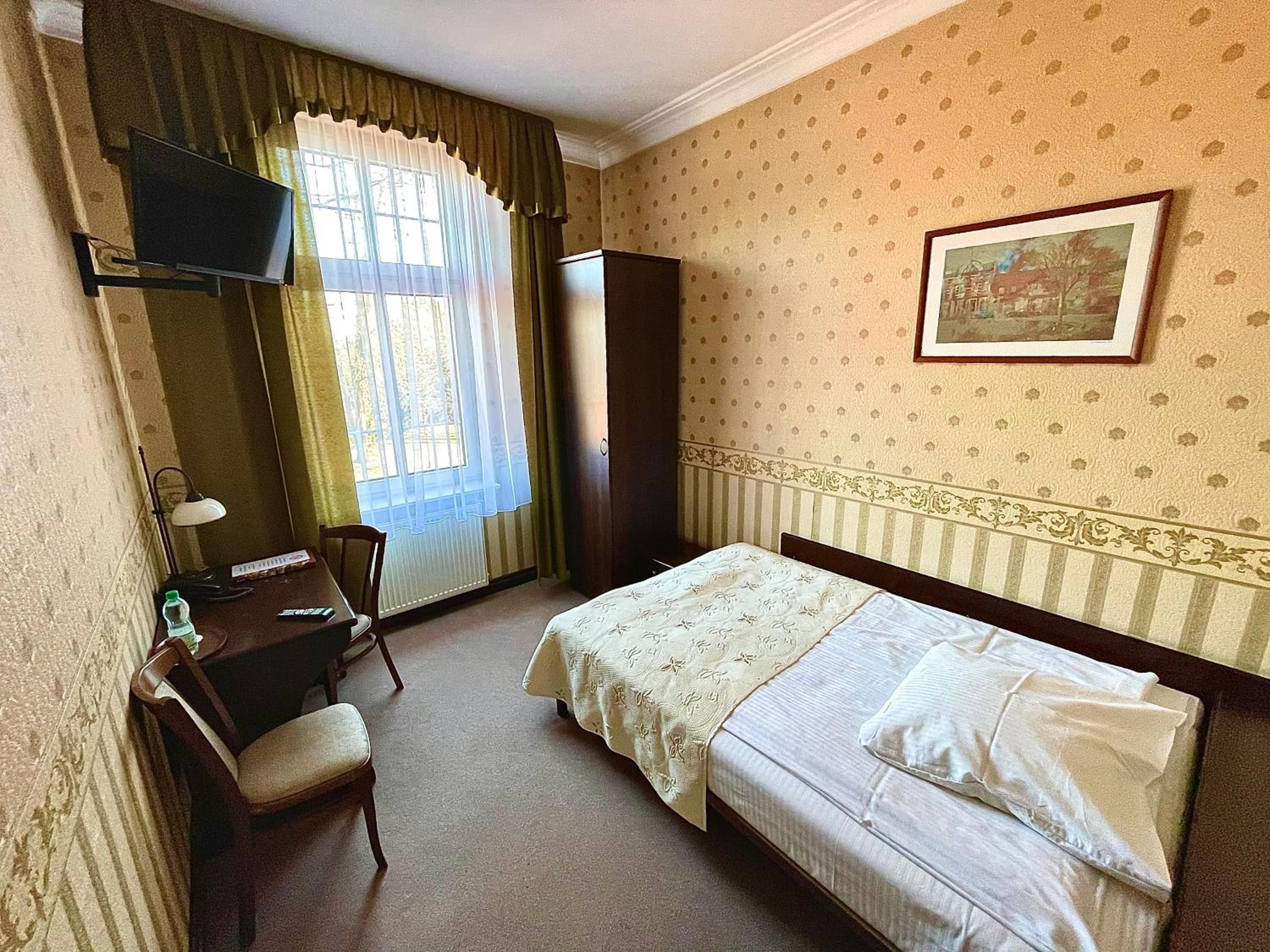 A hotel room with a bed, a desk, a chair, a television, and a window with curtains.
