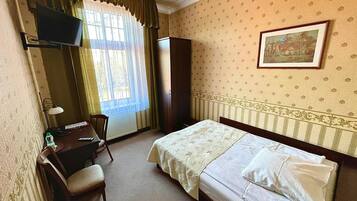 A hotel room with a bed, a desk, a chair, a television, and a window with curtains.