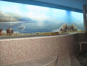 Un baño con piso de baldosas, un mural en la pared que representa un paisaje y un mostrador de baldosas.
