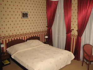A hotel room with a bed, a chair, a nightstand, a lamp, and curtains. - Pa Nska Gv Ra (Jaworzno)