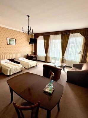 A hotel room with a dining table, two single beds, a sofa, a TV, and a window with curtains. - Pa Nska Gv Ra (Jaworzno)