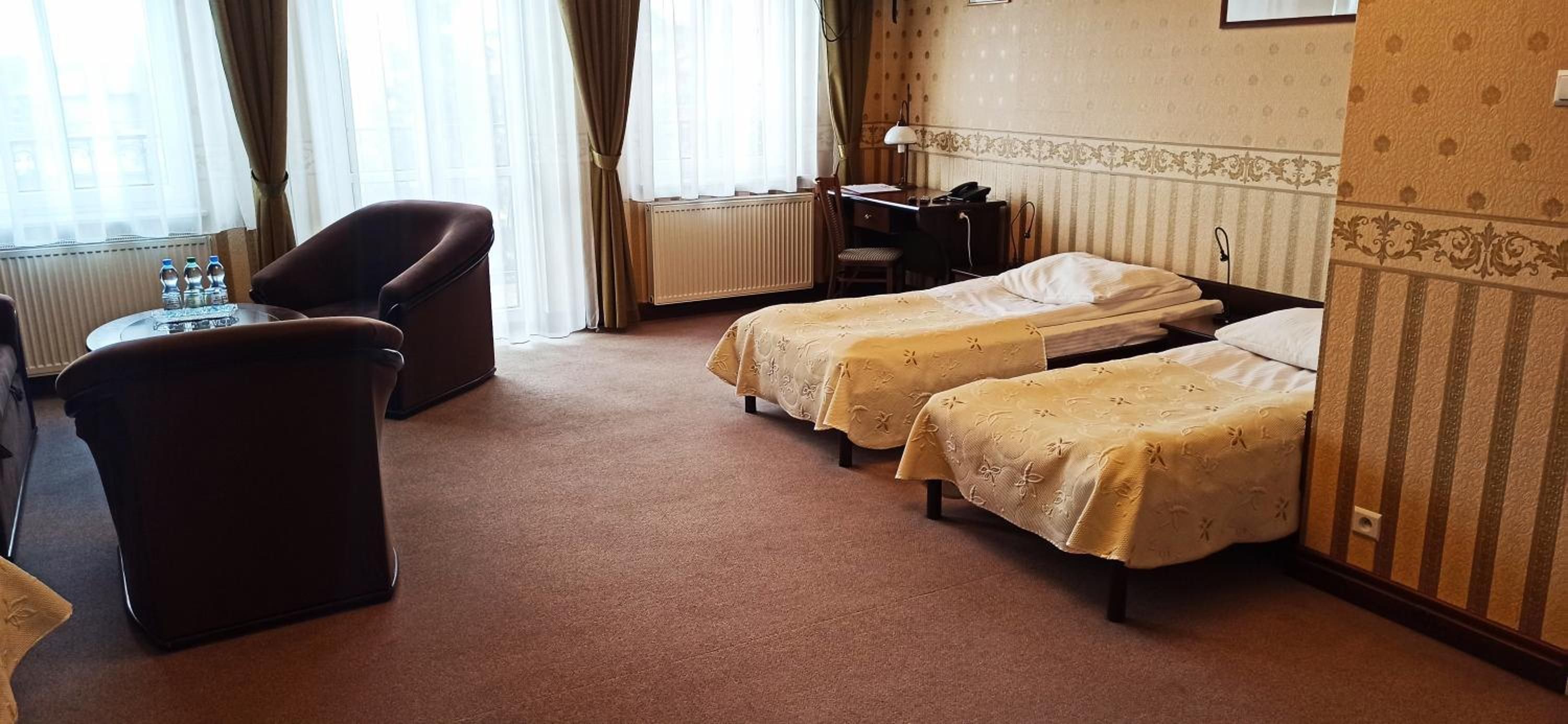 Ein Hotelzimmer mit zwei Einzelbetten, einem Schreibtisch, einem Stuhl und einer Heizung.