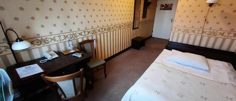 Une chambre d’hôtel comprenant un lit, un bureau avec un téléphone, une chaise, une lampe et un miroir.
