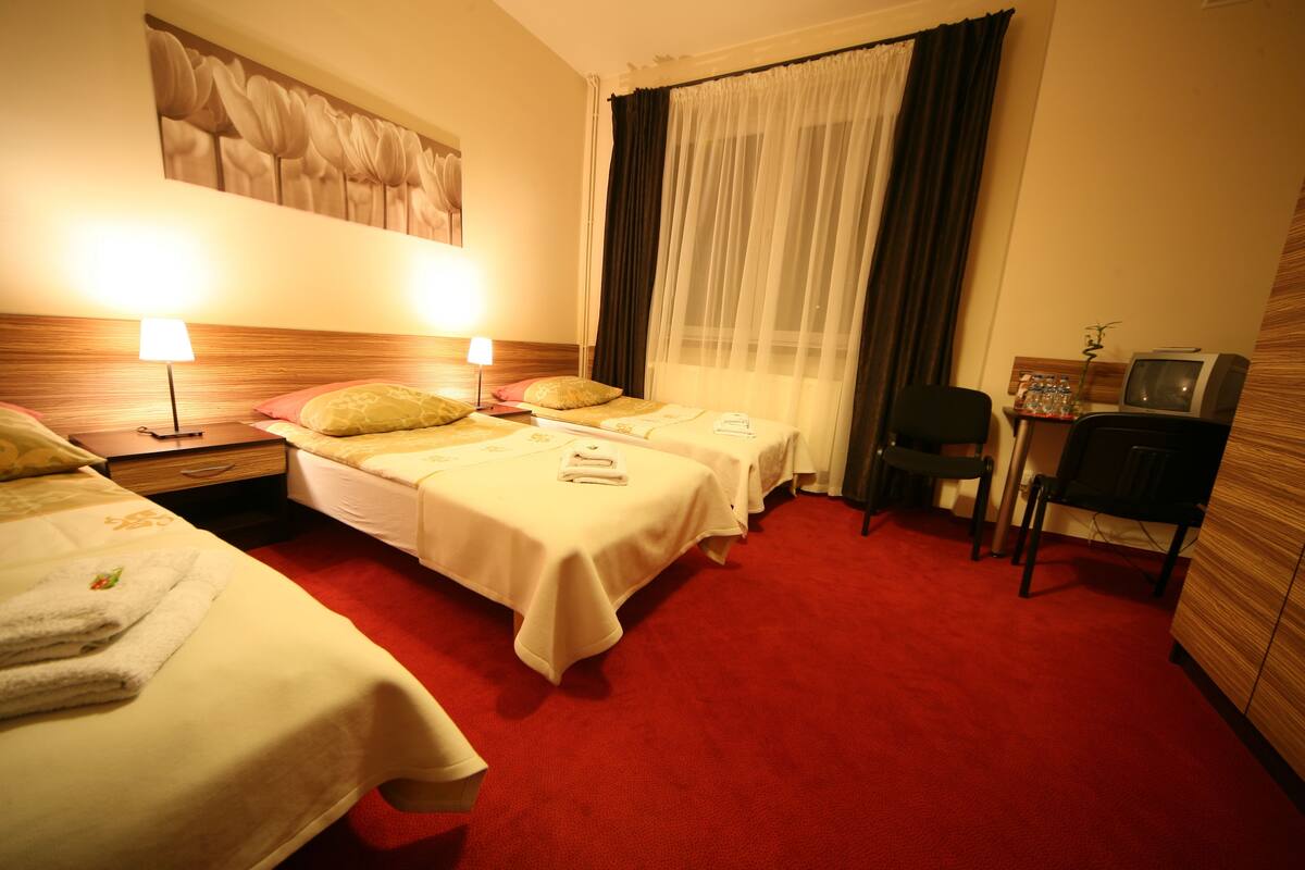 Une chambre d’hôtel avec deux lits, un bureau, une chaise, une télévision et une grande fenêtre avec des rideaux.