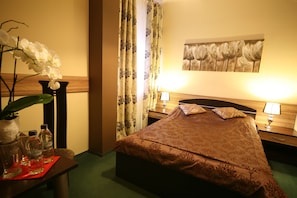 Quarto de hotel com cama, duas mesas de cabeceira, abajur, vaso com flores e um quadro na parede.
