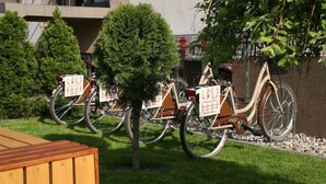 A row of bicycles parked in a grassy area with a wooden bench and a tree in the foreground. - Hotel Seven 7 (Kalisz)