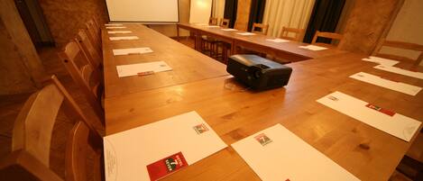 Un salón de conferencias con una larga mesa de madera, sillas, un proyector y documentos con el logotipo del hotel.
