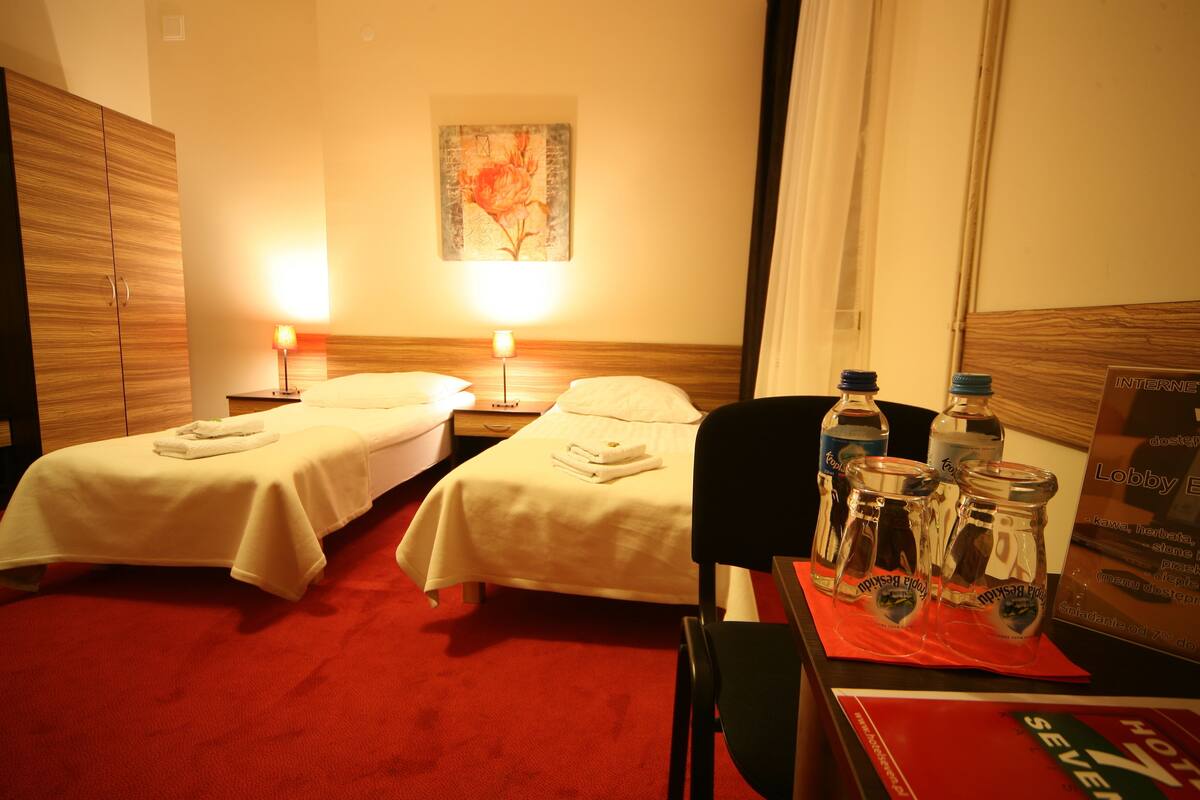 Une chambre d’hôtel avec deux lits, une table de chevet avec une lampe, une chaise et une table avec des bouteilles et un menu.