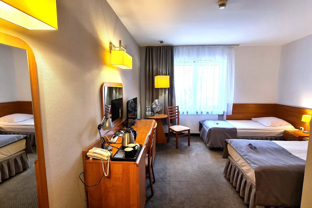 Une chambre d’hôtel avec deux lits simples, un bureau avec un téléphone, une chaise, une petite table et une fenêtre avec des rideaux.