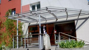 Um edifício moderno com marquise de vidro, escadaria e um vaso com plantas verdes.