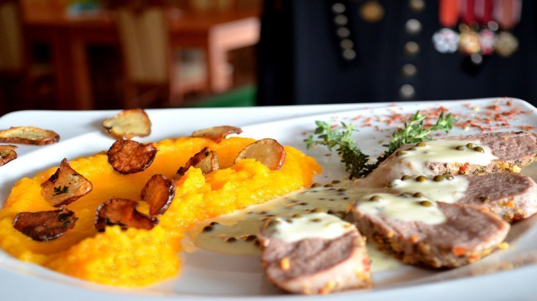 A plate with sliced meat, roasted potatoes, and a creamy sauce.