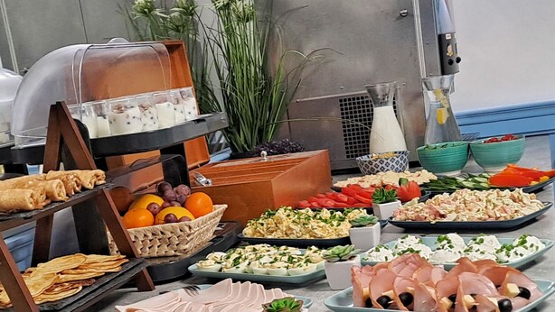Buffet com diversos alimentos, incluindo carnes, queijos, frutas e vegetais.