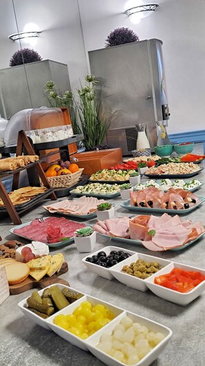 Een buffet met diverse gerechten, waaronder vleeswaren, kazen, fruit en groenten.