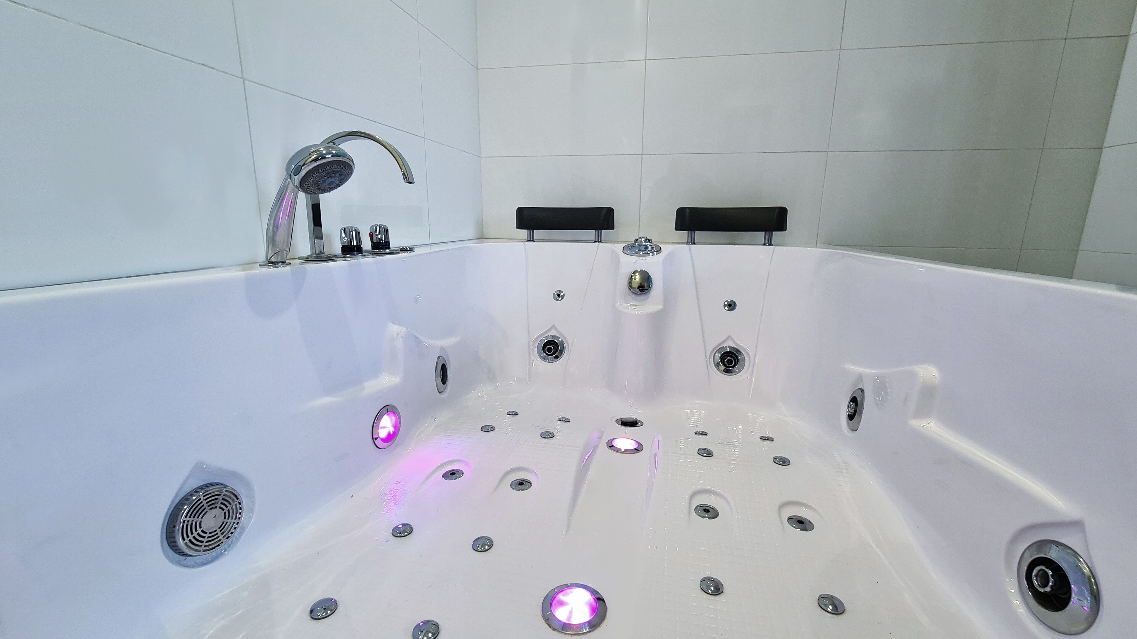 A white bathtub with a showerhead, multiple drains, and illuminated fixtures.