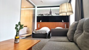 Quarto de hotel com cama, sofá, mesinha de madeira e vista para a cidade pela janela.