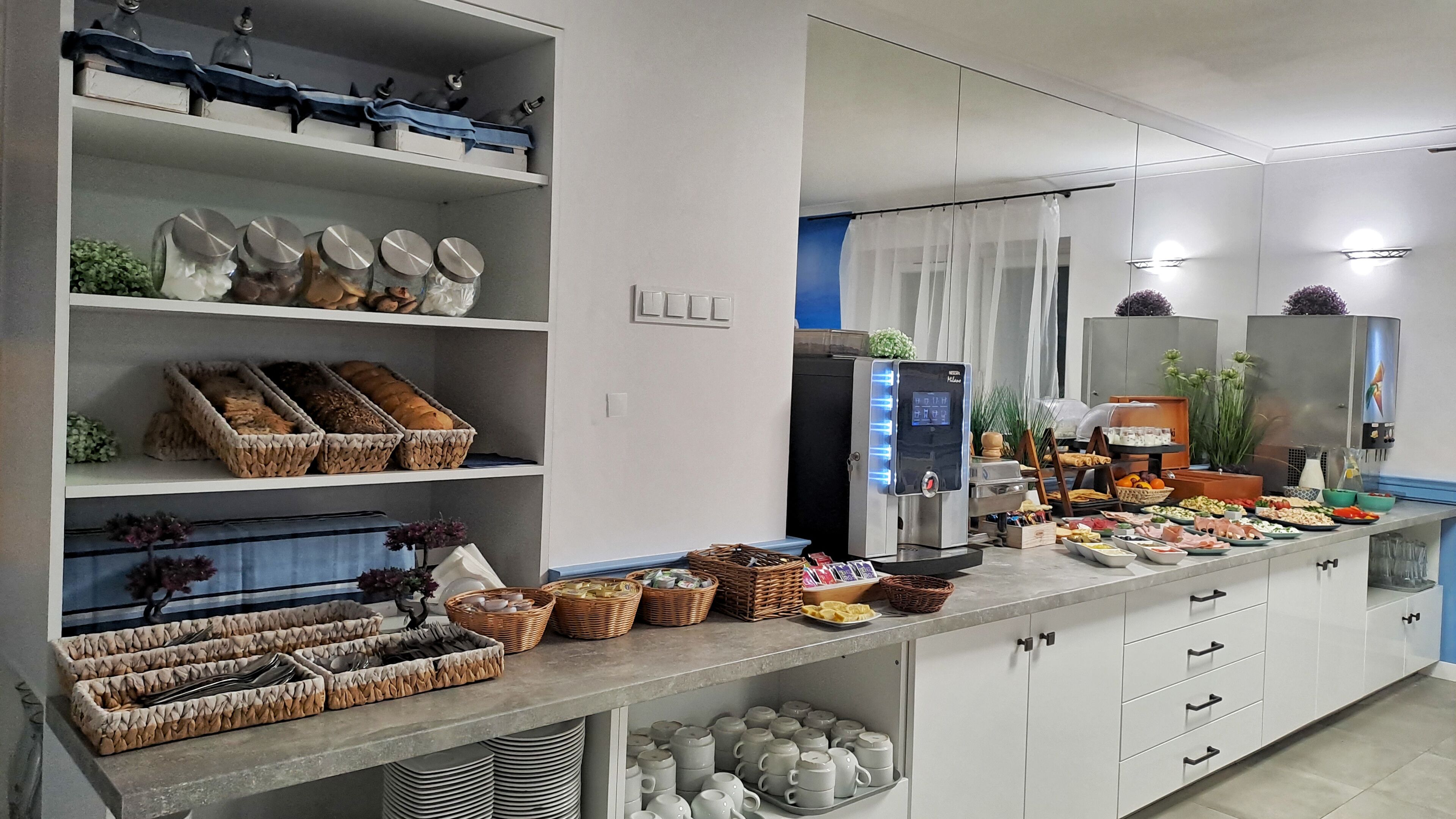 Cocina moderna con barra de desayuno tipo autoservicio, que incluye pan, bollería y una cafetera.