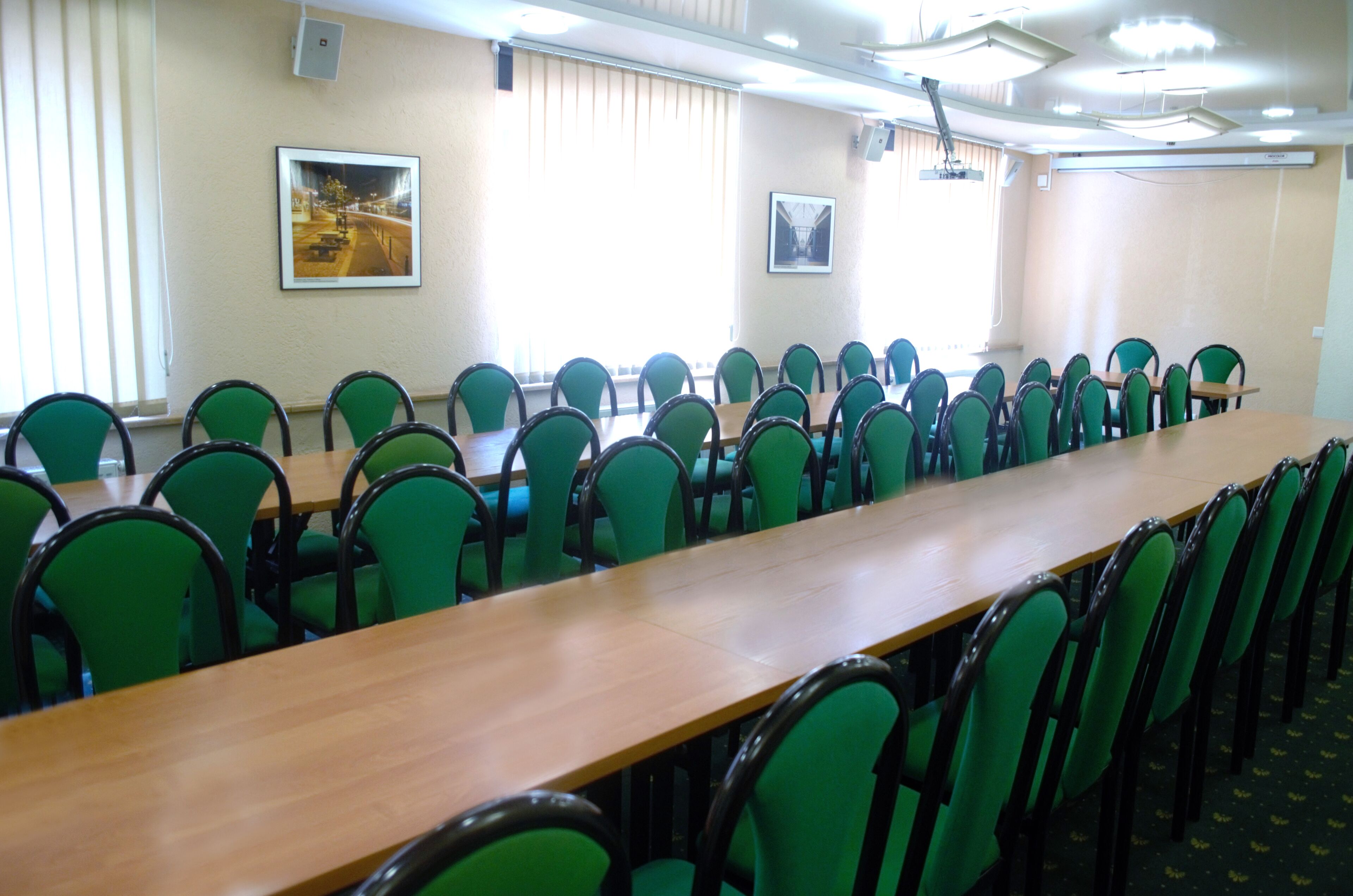 A conference room with a long table and green chairs, large windows with blinds, and framed pictures on the walls.