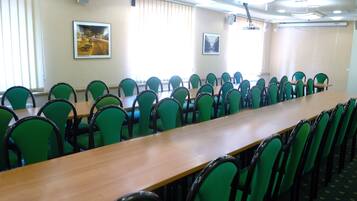 A conference room with a long table and green chairs, large windows with blinds, and framed pictures on the walls.