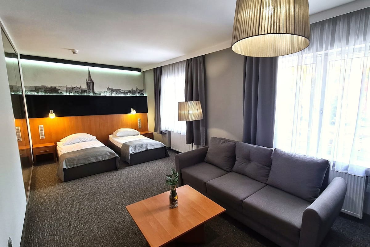Une chambre d’hôtel avec un canapé, deux lits simples, une table basse en bois et une fresque murale représentant un paysage urbain.