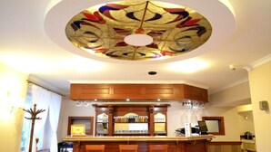 Uma área de bar com balcão de madeira, banquetas e teto com design em vitrais.