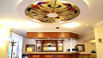 Zona de bar con mostrador de madera, taburetes y techo con diseño de vitral.