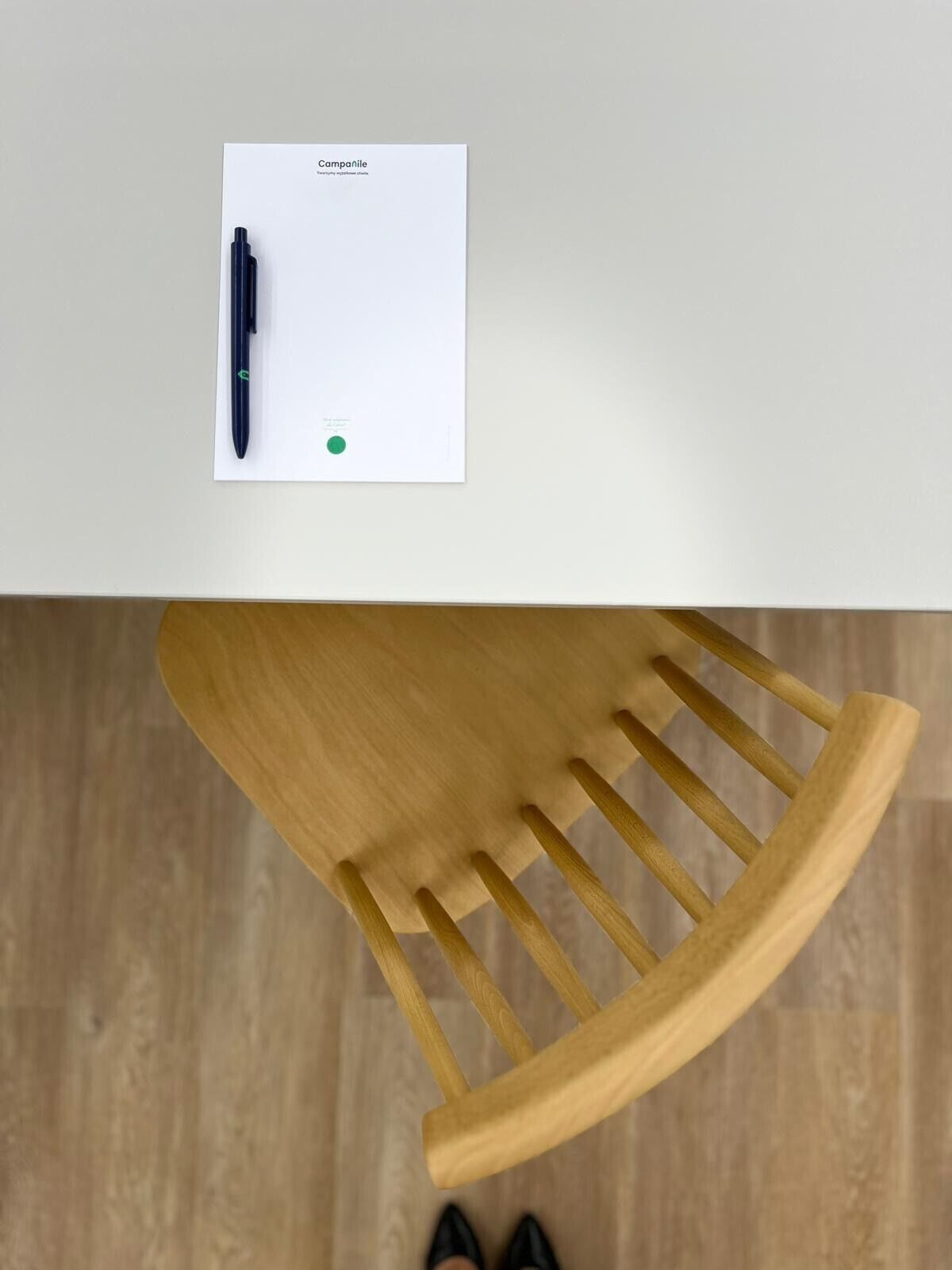 A top-down view of a wooden chair with a white table beside it, featuring a black pen and a green marker.