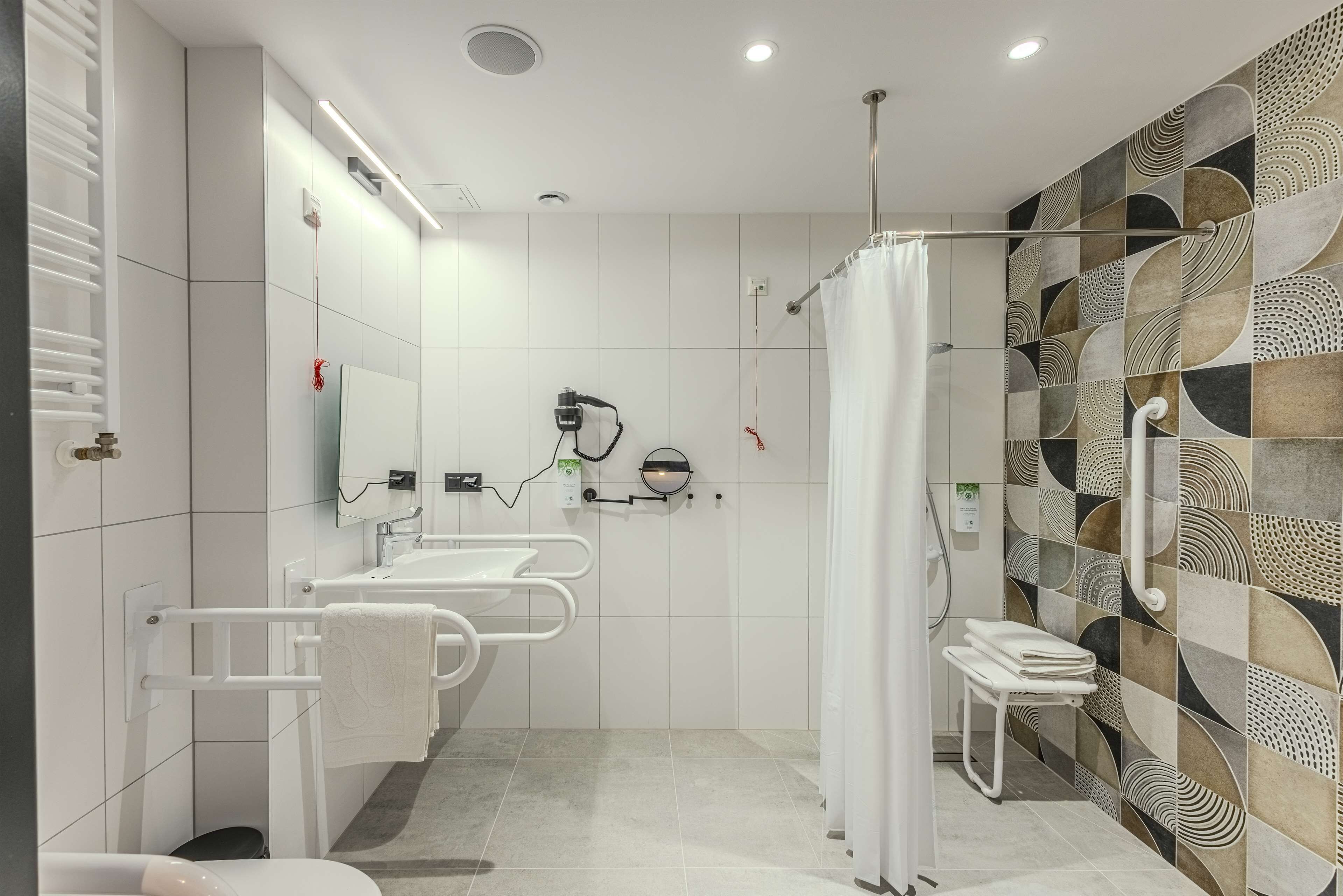 A modern bathroom with a shower, two sinks, a towel rack, and a patterned wall.