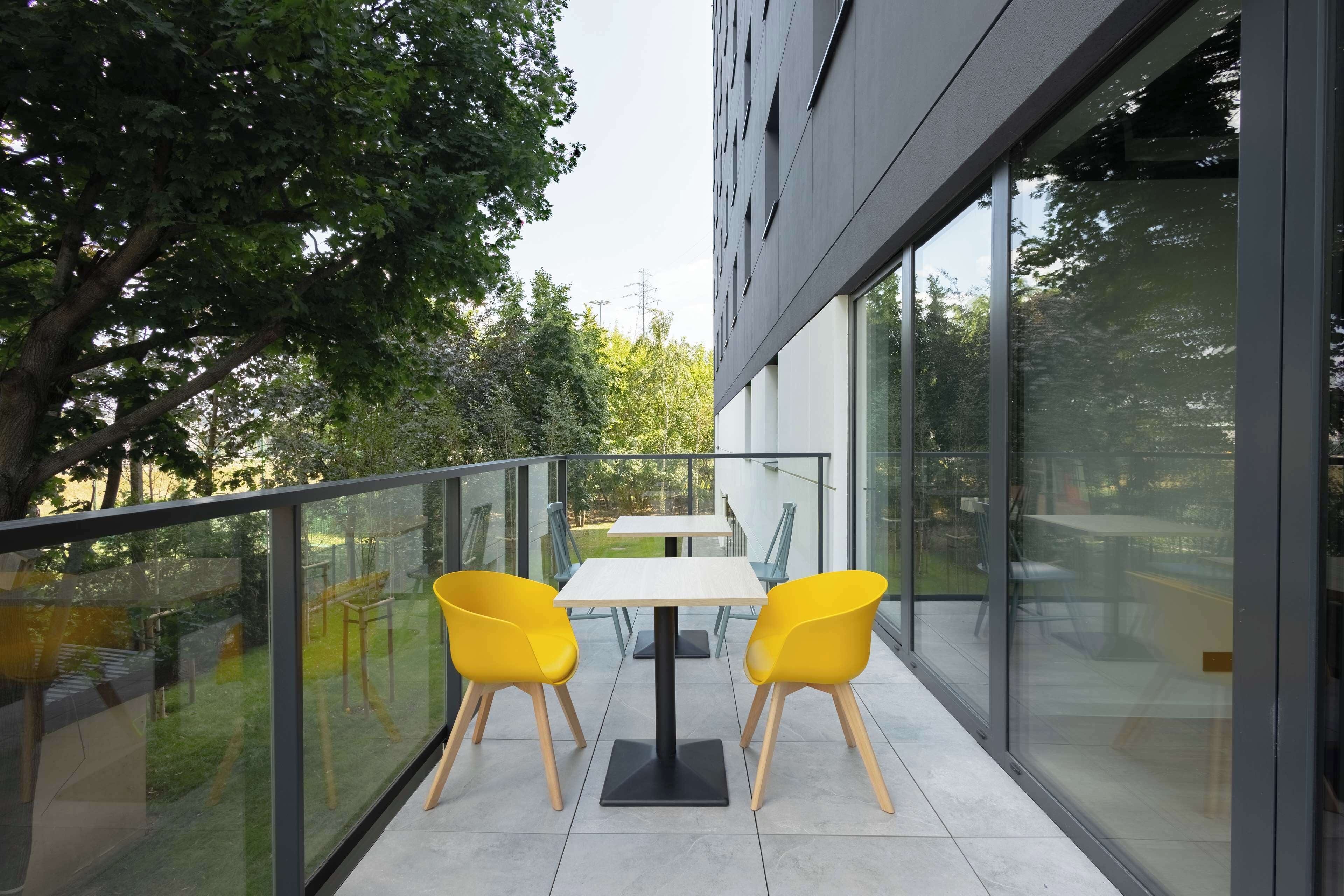 Un balcone con un tavolo e due sedie, vista su un giardino e un edificio.