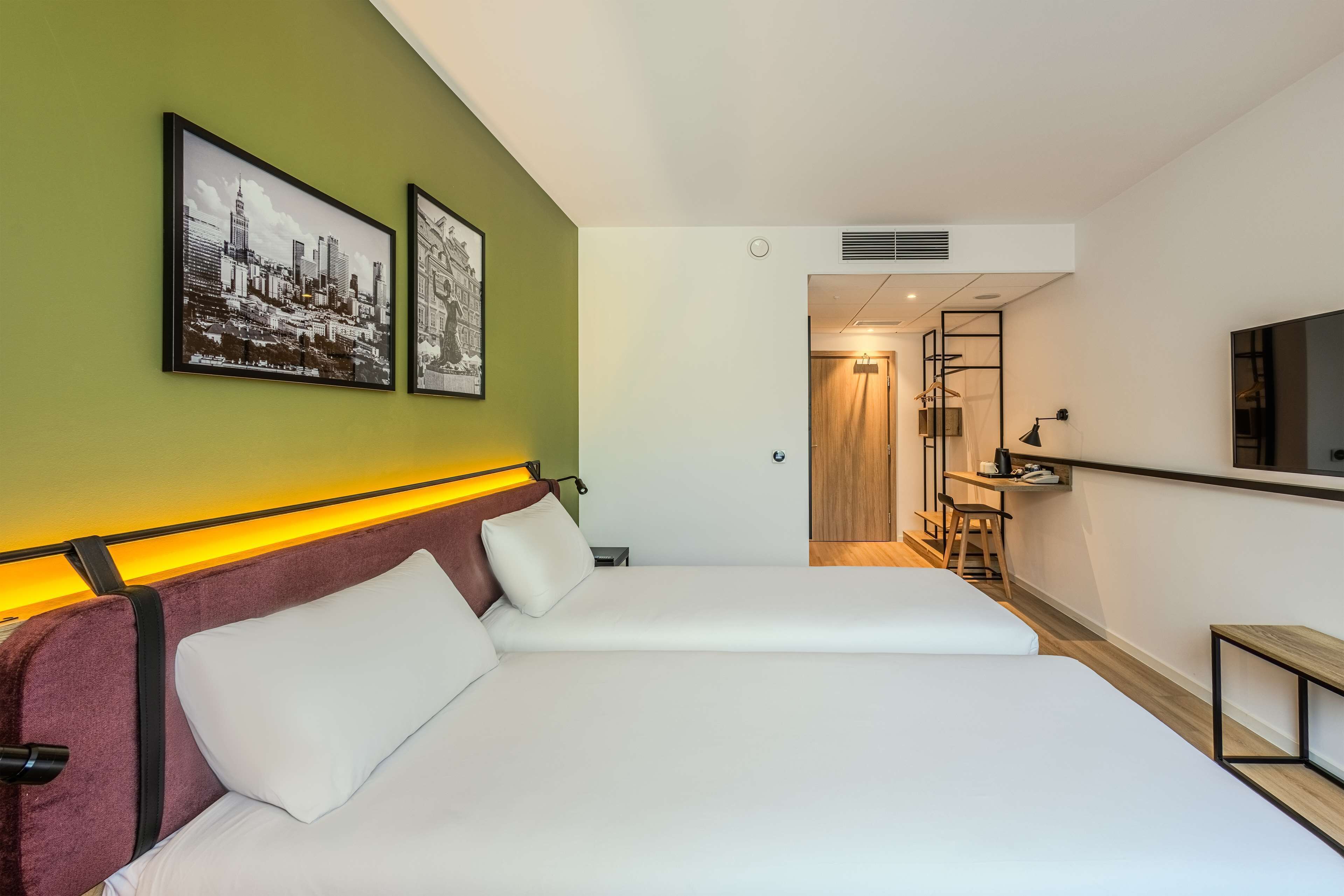 A hotel room with two beds, a television, and artwork on the wall.