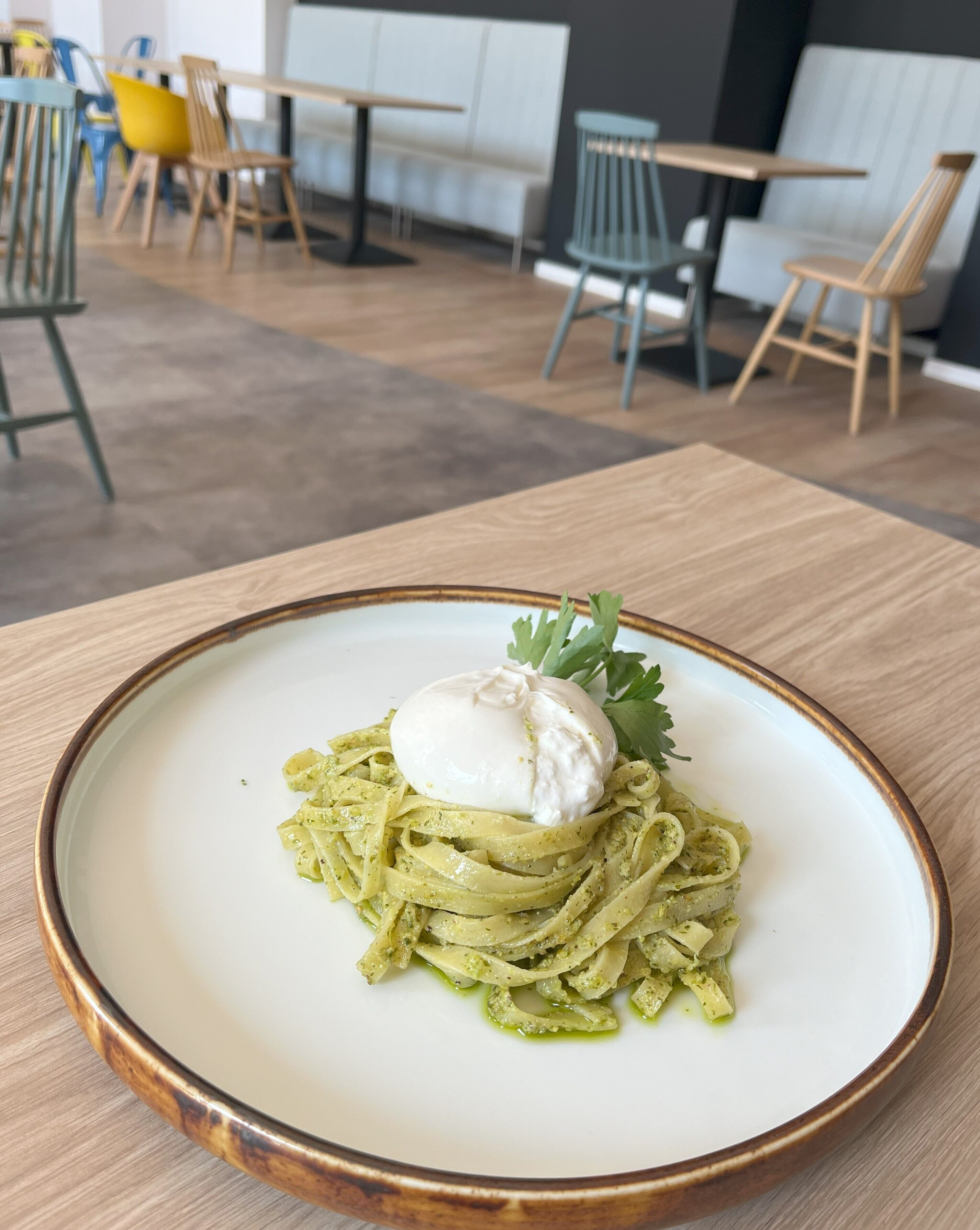 A plate of pasta with a poached egg and garnish on a table in a dining area with chairs and tables.