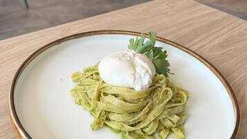 A plate of pasta with a poached egg and garnish on a table in a dining area with chairs and tables.
