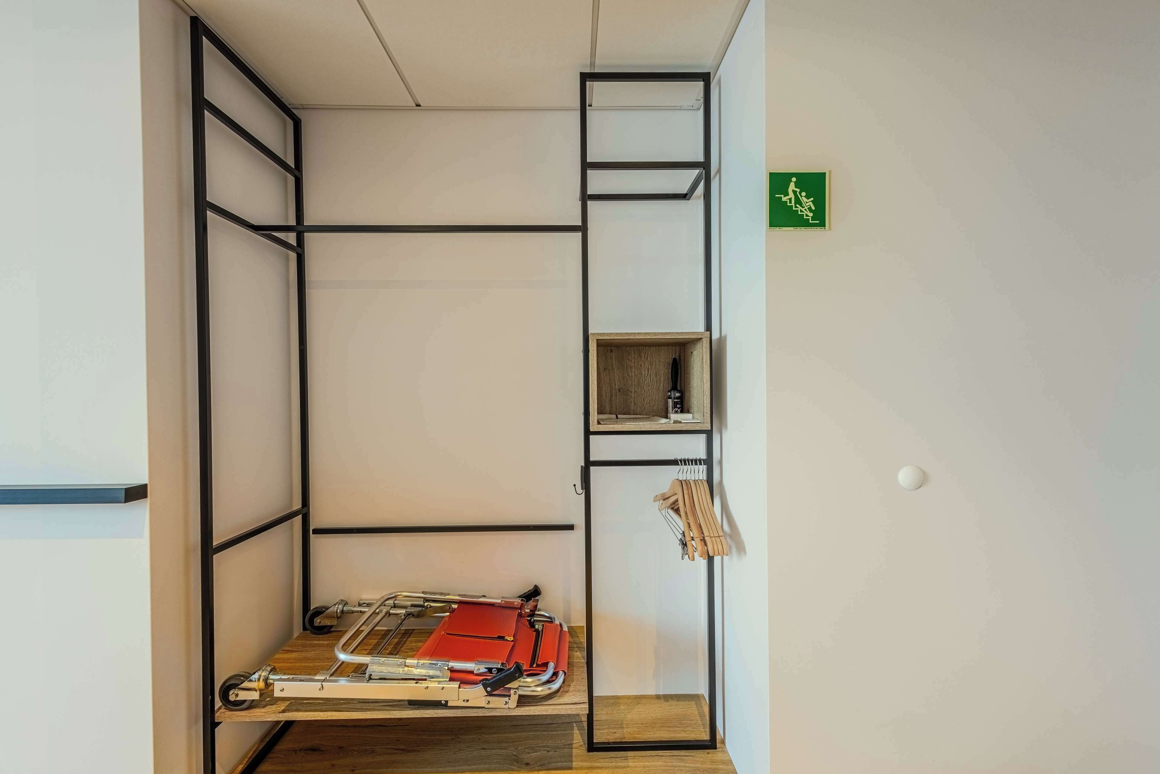 Une pièce de taille modeste, équipée d’un lit pliable, d’une petite étagère et d’un panneau vert fixé au mur.