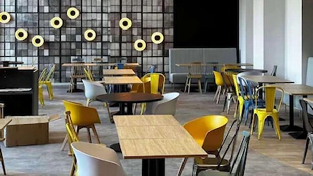 A modern dining area with multiple tables and chairs, a patterned wall, and pendant lighting. - Campanile Warszawa Polnoc (Warsaw)