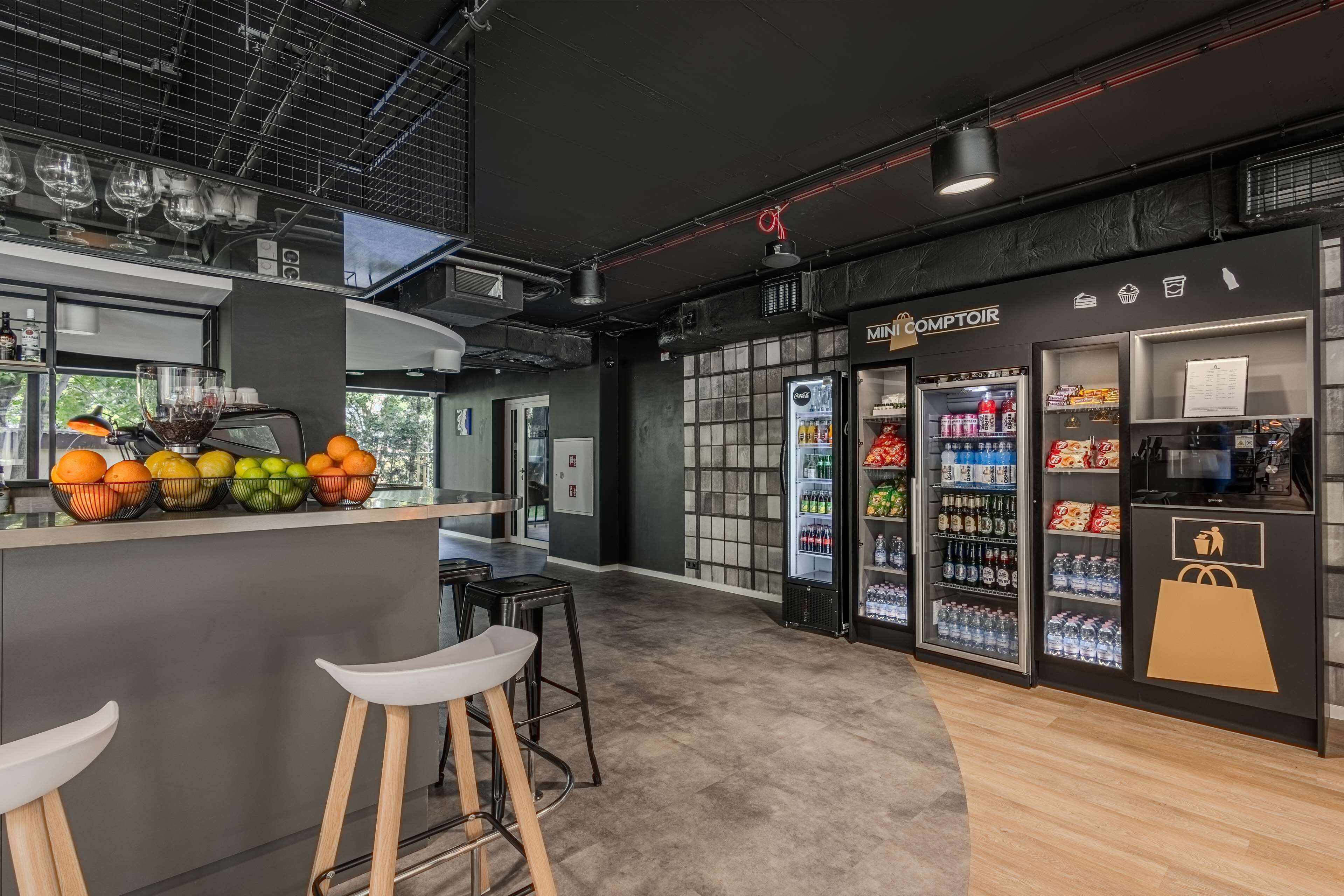 A modern bar area with stools, a refrigerator stocked with beverages, and a counter with a variety of snacks.