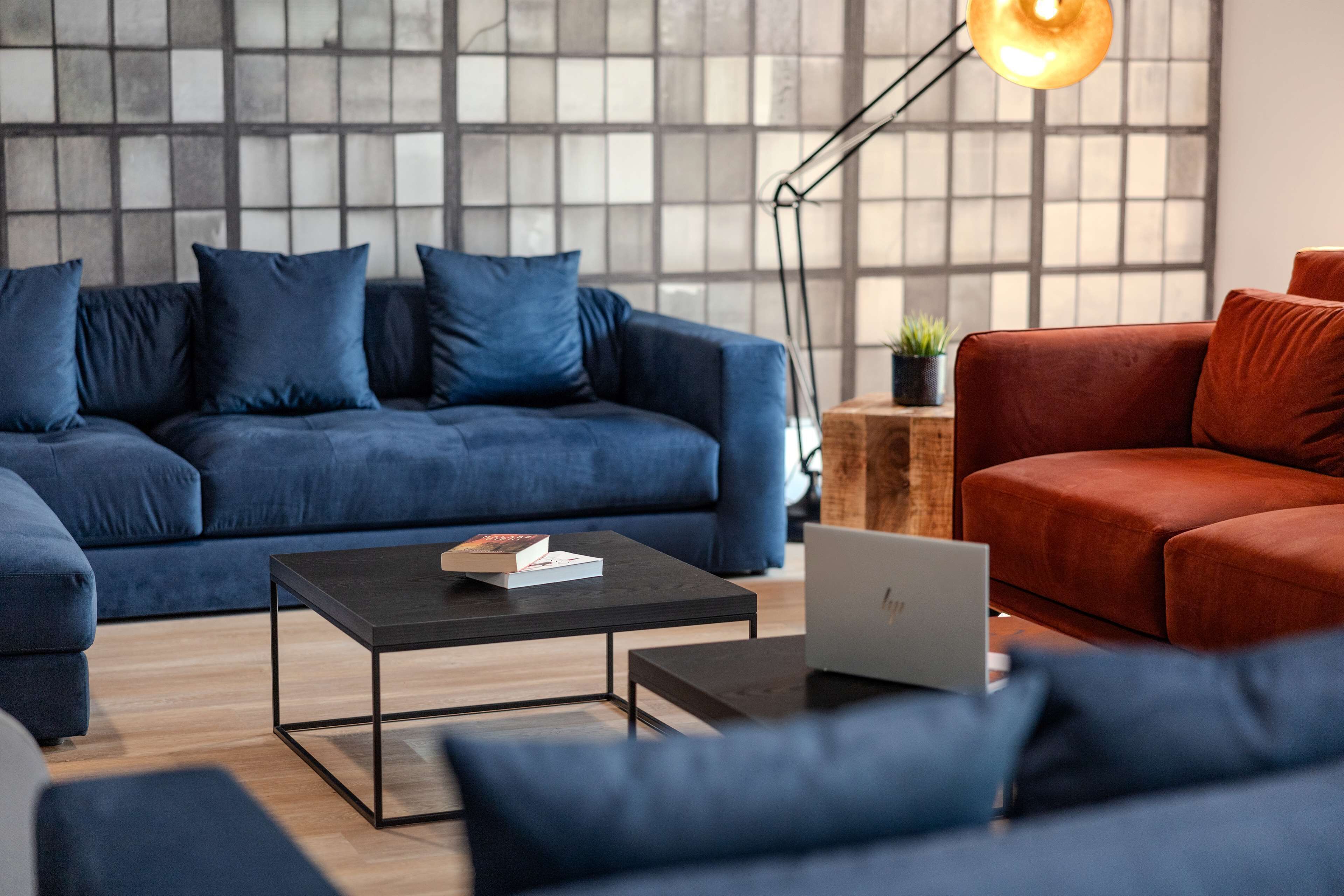 Ein modernes Wohnzimmer mit einem blauen Sofa, einem roten Sofa, einem schwarzen Couchtisch und einem Laptop auf Holzdielen.