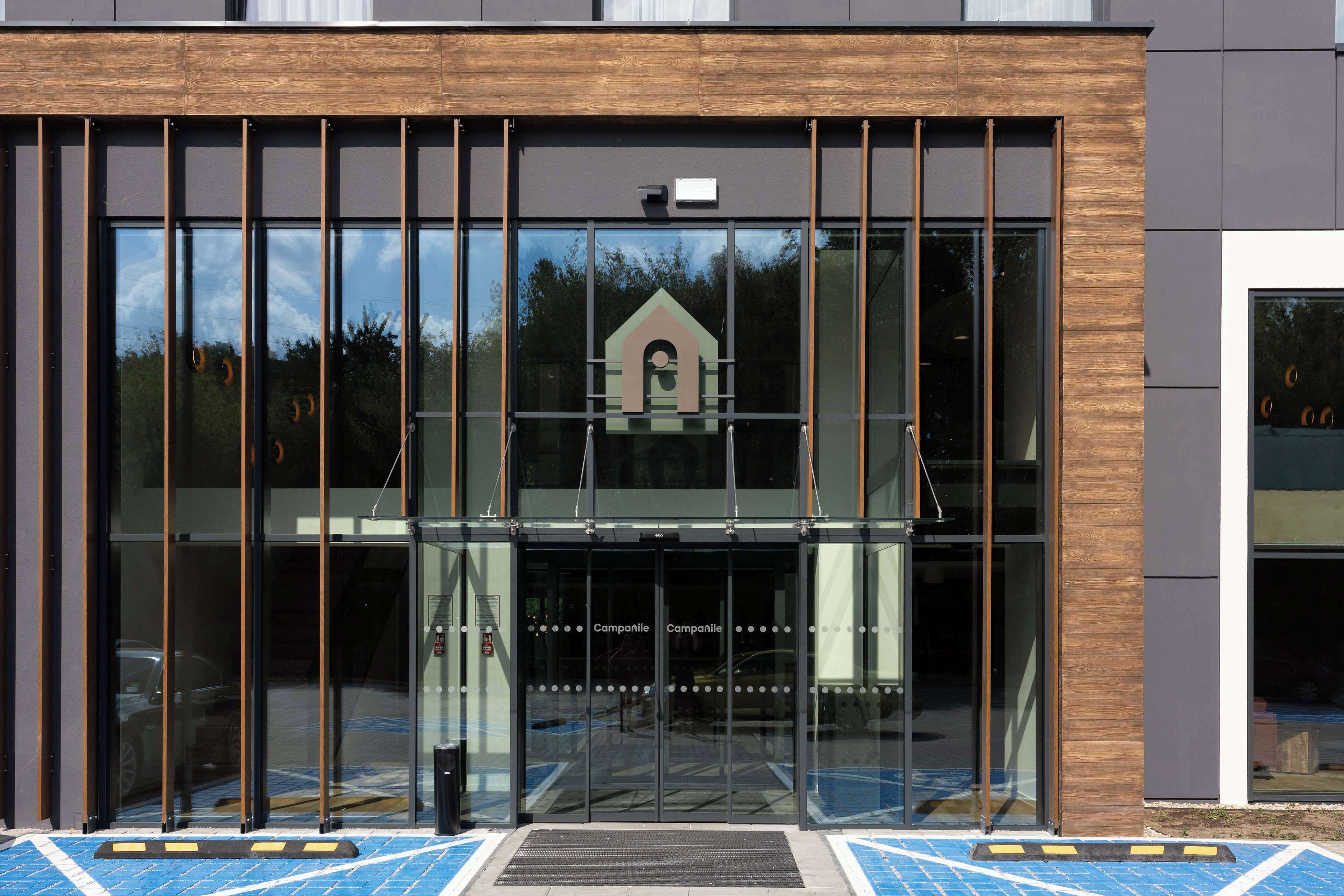 Een moderne gevel met grote glazen deuren, een houten bekleding en een klein raam in de vorm van een huis.
