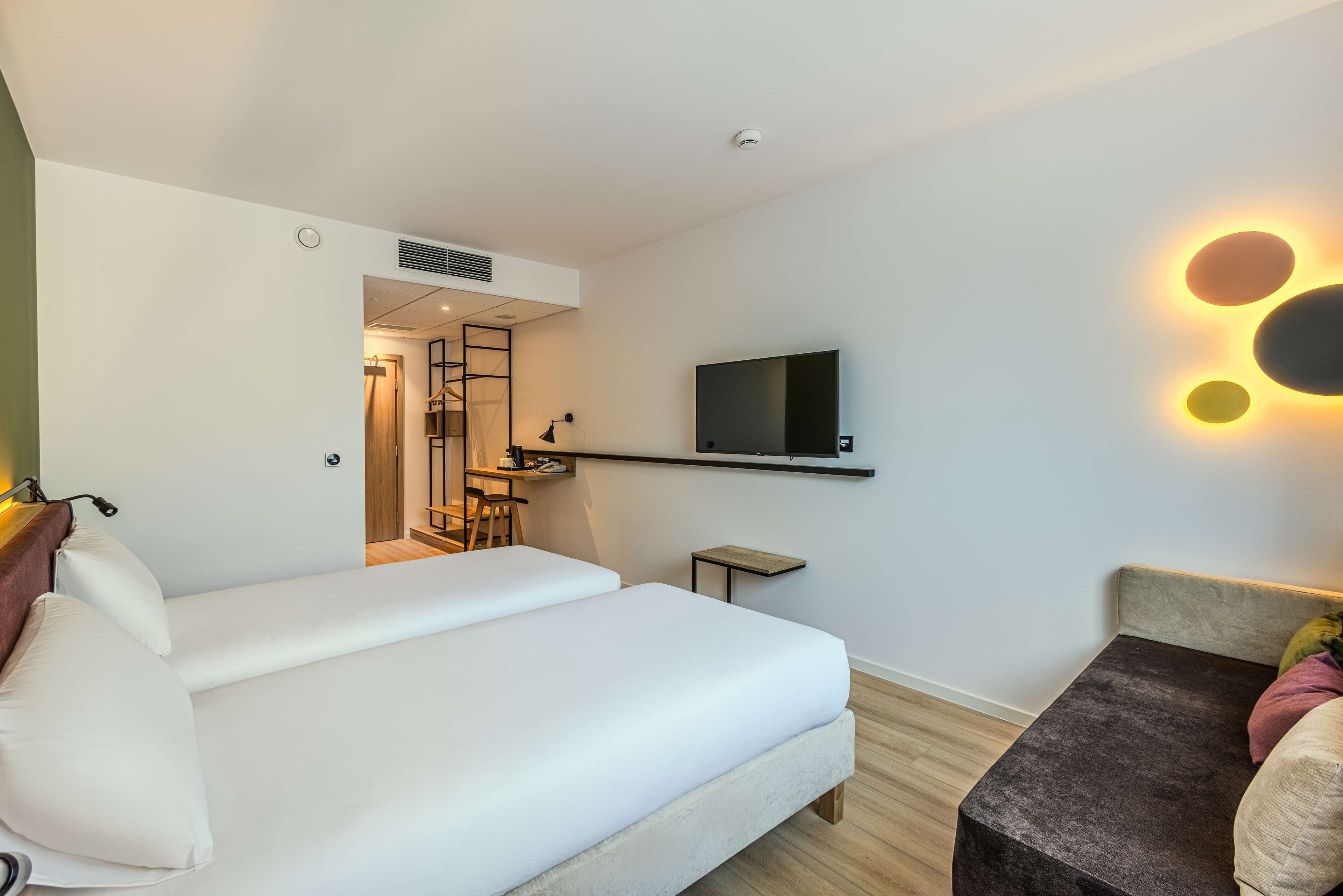 A hotel room with a bed, a desk, a TV, and a seating area.