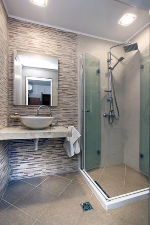 Un baño moderno con cabina de ducha de vidrio, un lavamanos con espejo y suelo de baldosas.