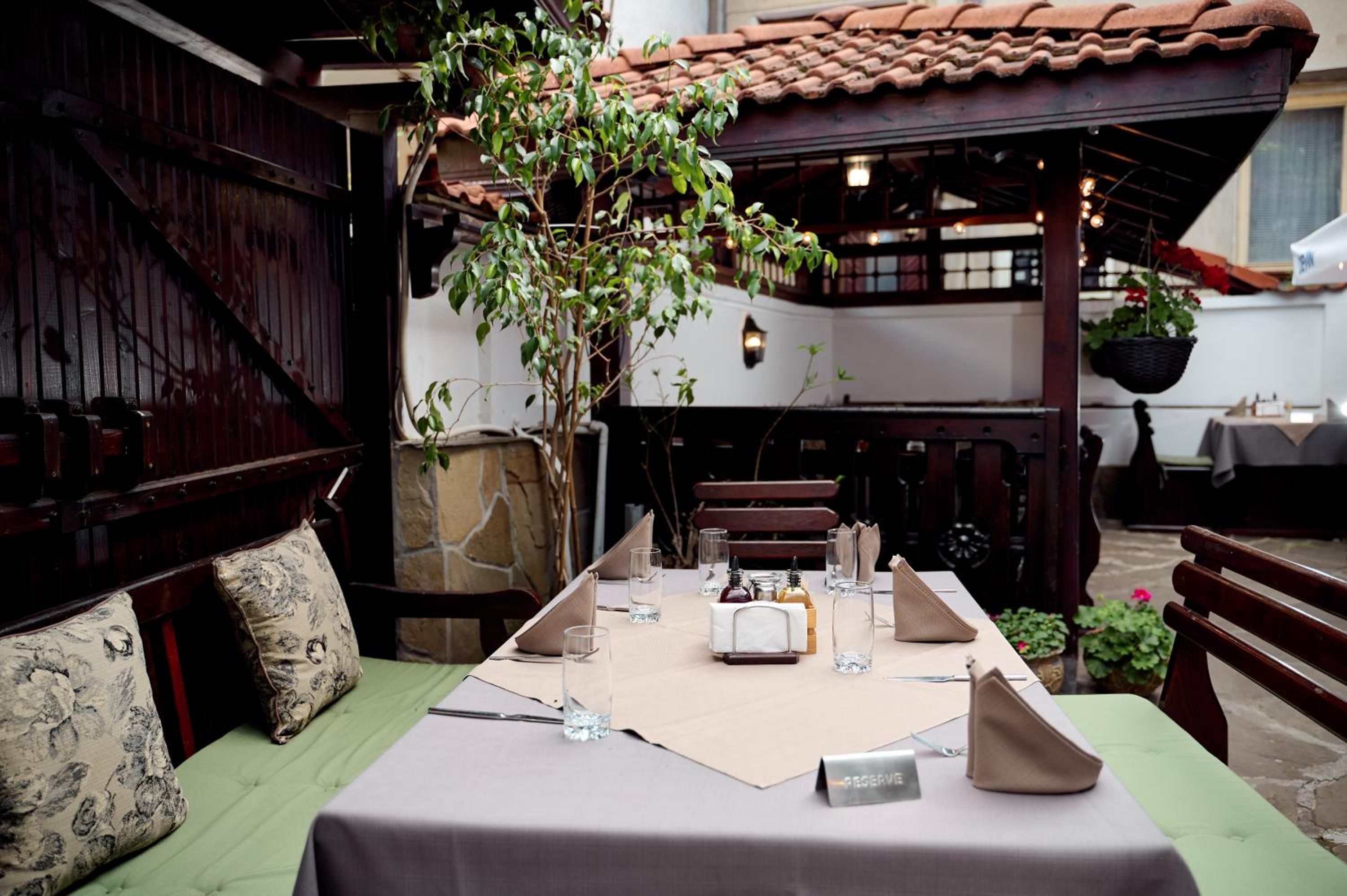 Un comedor con una mesa para dos, un banco y una pérgola con un árbol.