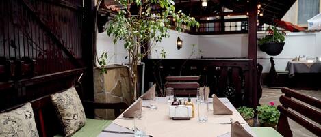 Un comedor con una mesa para dos, un banco y una pérgola con un árbol.