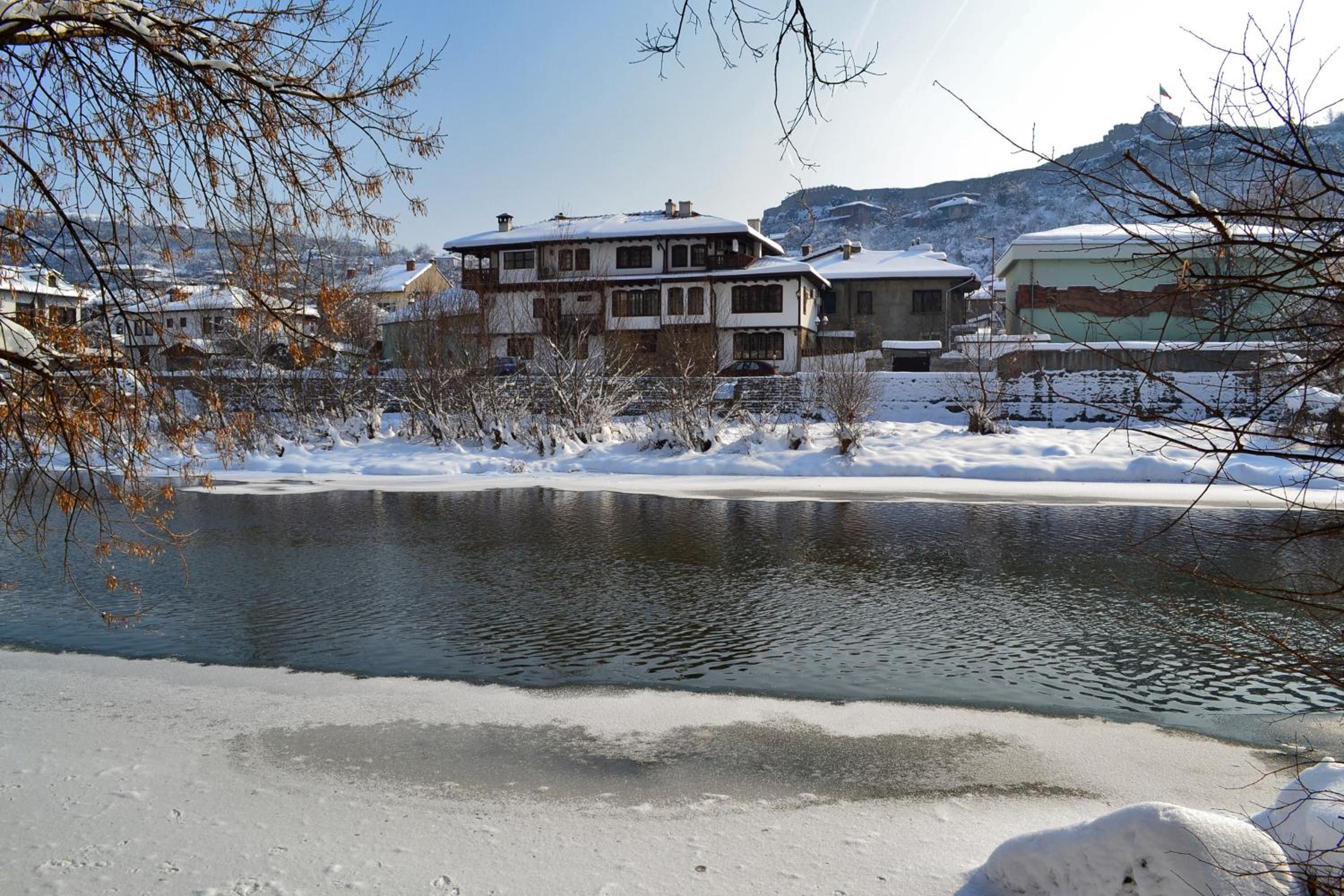 Una zona residencial con una casa grande, un estanque y alrededores cubiertos de nieve.