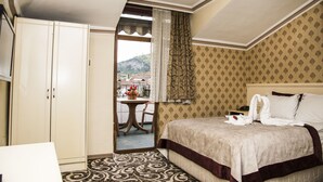 A hotel room with a bed, a wardrobe, a table with chairs, and a view of a mountain. - Nazar Hotel (Trabzon)