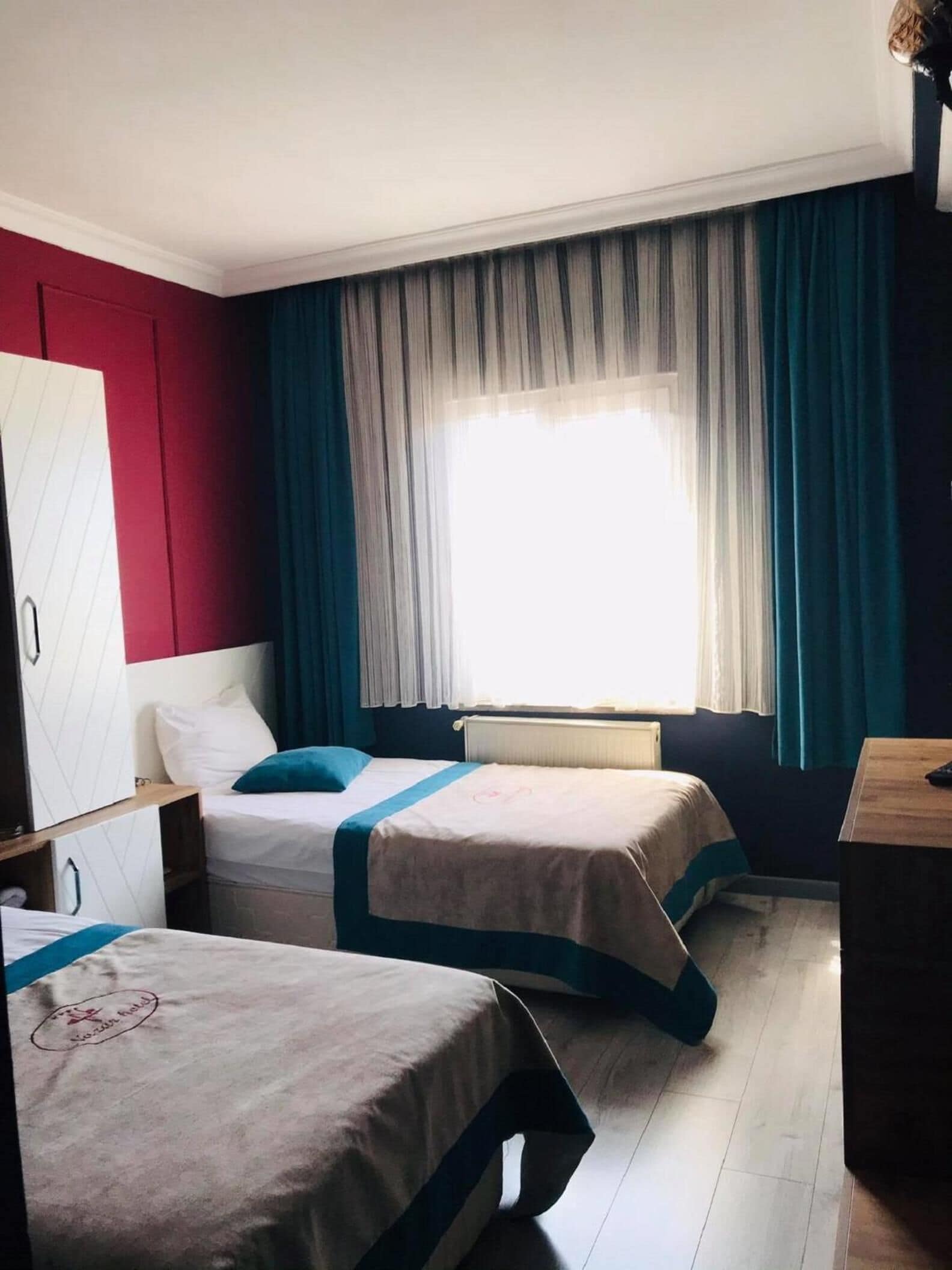 Ett hotellrum med två sängar, en garderob, ett skrivbord och ett fönster med gardiner.
